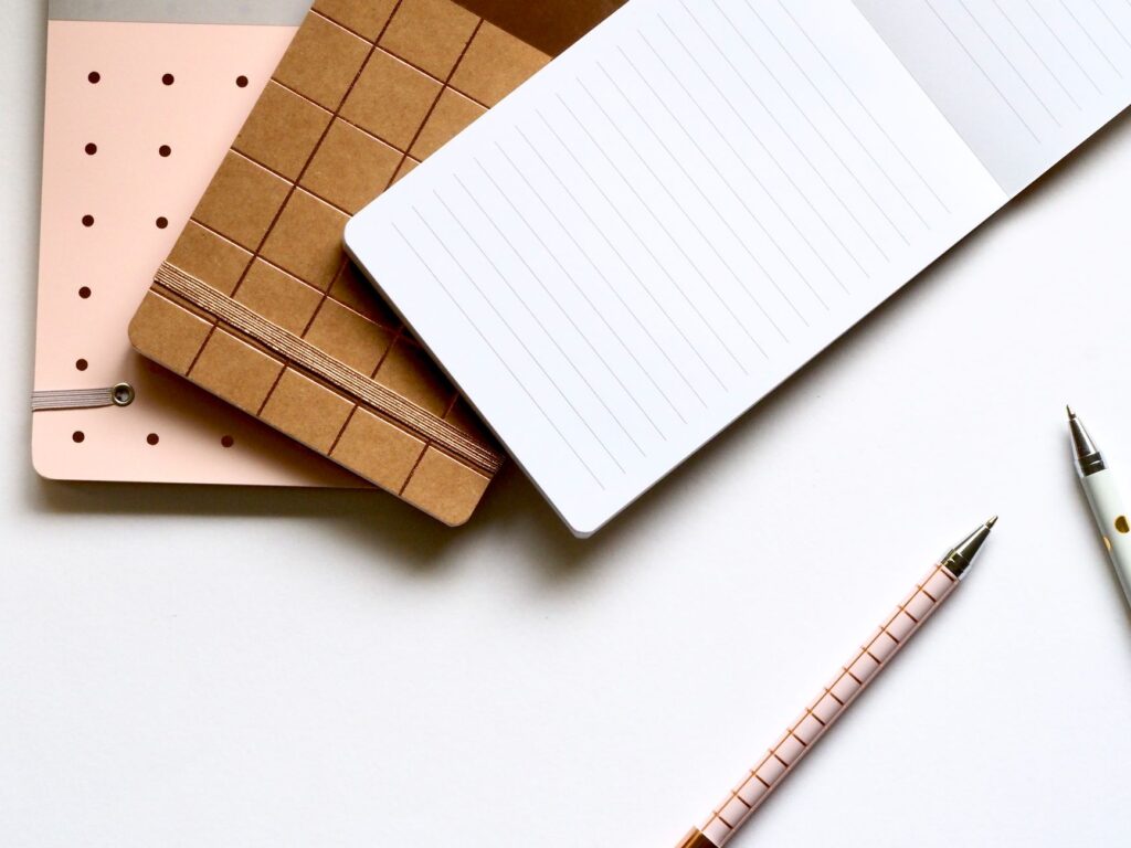 A minimalist flat lay featuring stylish notebooks and pens on a white background.