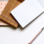 A minimalist flat lay featuring stylish notebooks and pens on a white background.