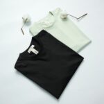 Two cotton t-shirts in black and mint green on a light background with cotton flowers.